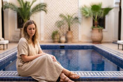 Femme en robe de lin contemplant la piscine d'un riad marocain
